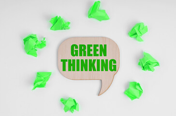 On a white background, there are crumpled green pieces of paper and a wooden sign with the inscription - Green Thinking