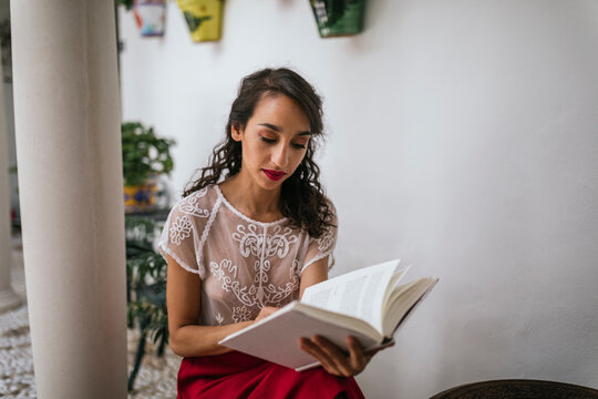 Ethnic woman reading book in patio