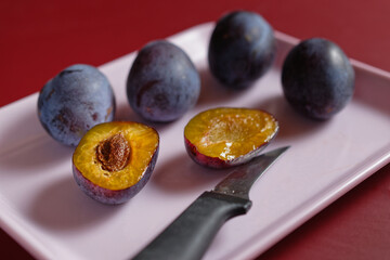 One halved and whole plums on small pink tray