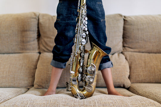 Unrecognizable girl with saxophone on couch in house