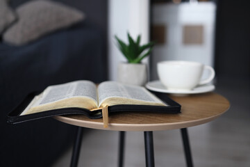 Open Bible with a cup of tea on a wooden table in the bedroom. Time for prayer.