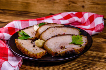 Slices of baked pork belly, garlic and parsley on a black plate