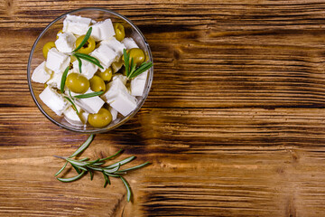 Chopped feta cheese, rosemary and olives in glass bowl on a wooden table. Top view