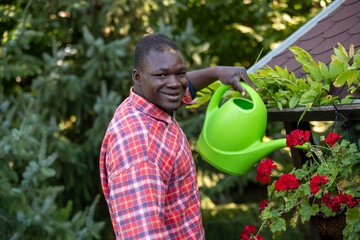 Handsome youg man watering red geraniums outdoors.