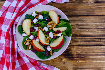 Salad with spinach leaves, feta cheese, cranberries, walnuts and apple in a ceramic plate. Top view