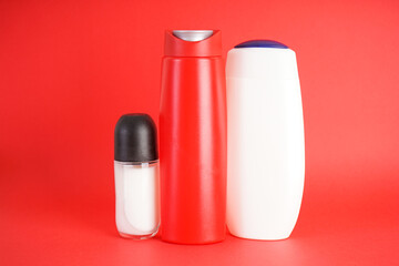 Set of bottles of shampoo and deodorant on a red background.