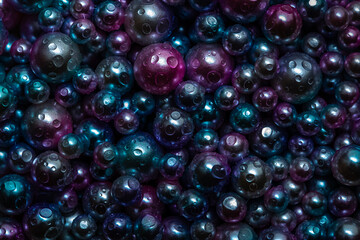 Beautiful background with nacreous dark pearls, top view. Abstract texture for festive backgrounds. Shiny multicolored dark surface of Christmas decorations. Gems close-up. Black bright background.