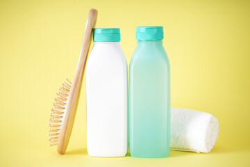 Shampoo, bottle of hair conditioner and wooden hair brush on a yellow background.