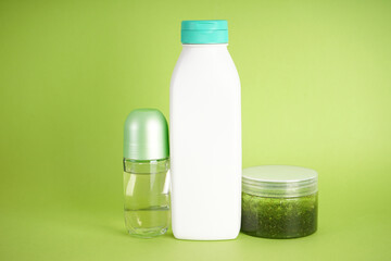 White bottle of shampoo, body scrub and deodorant on a green background.