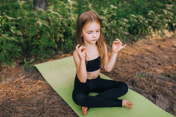 Hardworking, cute, preschool girl, child athlete sits on a green rug in a lotus position, legs...