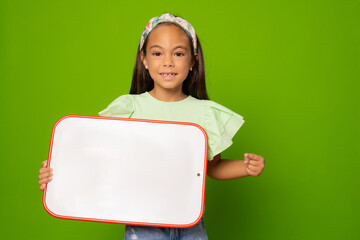 Cheerful little child girl holding whiteboard over green background. Education and school concept.
