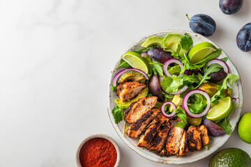 Grilled chicken fillet salad with arugula, avocado, plums, paprika, onion and lime in a plate on white background. Top view