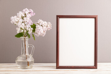 Fototapeta na wymiar Wooden frame with lilac flower in glass on gray pastel background. side view, copy space.