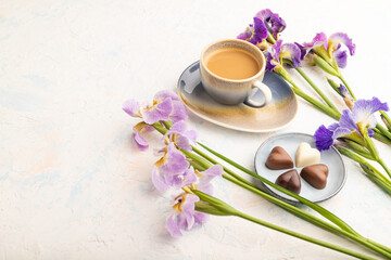 Obraz na płótnie Canvas Cup of cioffee with chocolate candies and lilac iris flowers on white concrete background. side view, copy space.