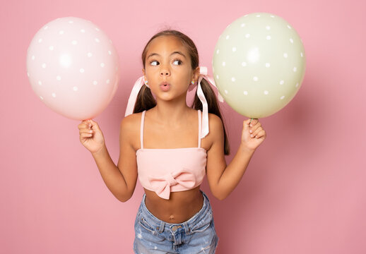 Beautiful little girl with pastel colors air balloons isolated over pink background.
