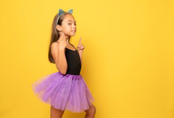 Beautiful little girl in Halloween costume pointing fingers up isolated over yellow...