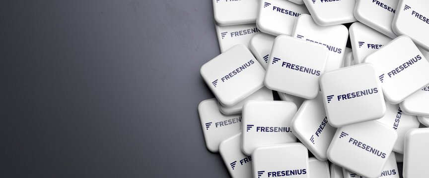 Logos of the German health care company Fresenius on a heap on a table. Copy space. Web banner format.