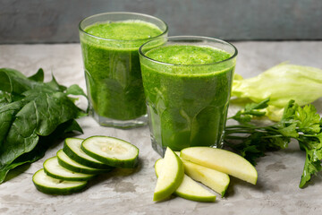 Green juice and ingredients in glass on grey background