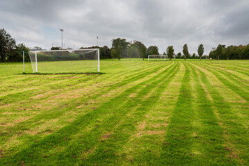 White metal soccer or football goal post and freshly cut training pitch. Cloudy sky. Simple sport background. Nobody. Cut green grass on a field.