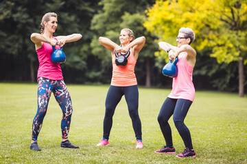 Group of happy healthy and fit women doing a kettle bell exercise in the park