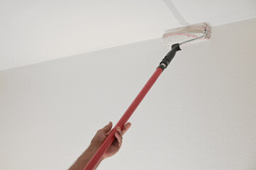 Hand of a man holding a paint roller on a long telescopic pole to paint the ceiling while renovating an apartment, housing concept, copy space, selected focus - obrazy, fototapety, plakaty