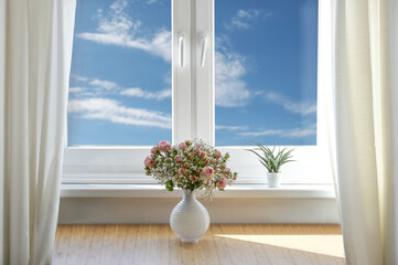 romantic flower bouquet with roses and baby's breath in a white vase on a table by the window with blue sky and clouds, copy space