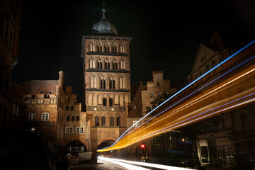 Light traces of a bus driving through the Burgtor gate tower of Lubeck at night, historic brick building of the former city surrounding wall in the old town, Schleswig-Holstein, Germany, copy space