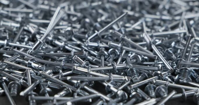 Aluminum rivets fall onto a rotating pile of metal rivets. Close-up.