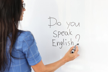 Woman teacher writes with marker do you speak english on white board