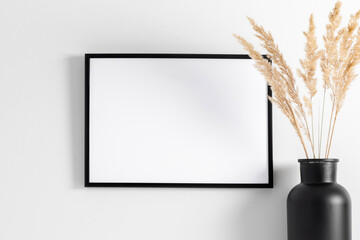 Black photo frame mockup on wall with reeds decoration 