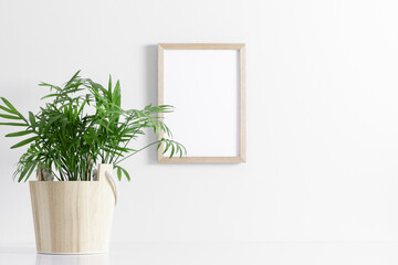 Wooden photo frame mockup on wall and palm plant on white table