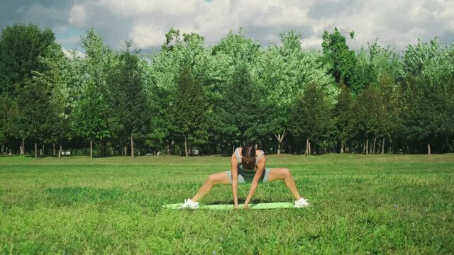 A beautiful sportive girl is engaged in yoga on green grass in a city park. Leg-split. Outdoor fitness and life balance concept. Slow motion. 4k footage.