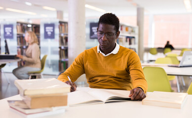 Intelligent african-american male student engaged in research working with books in university library. High quality photo