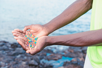 Hands full of microplastics on the beach. Different plastic colored ... Plastic pollution concept.