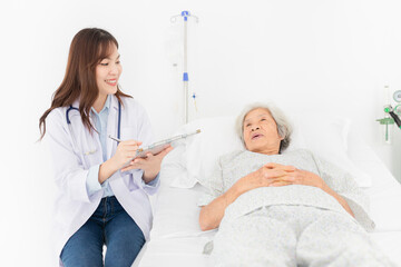 asian female doctor talk with old patient in hospital, she screening and write patient information on patient chart, elderly healthcare treatment