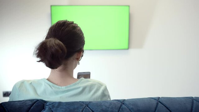 cinematic Girl Sits in Font of a Geen Sreen TV and uses phone, Green Chroma Key Screen TV, Relaxing on a Couch
