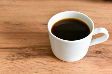 White cup of strong black coffee on wooden surface close up