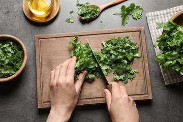 Woman cutting fresh green cilantro at grey table, top view