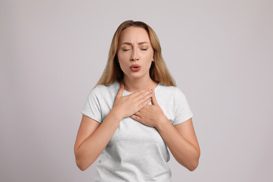 Young woman suffering from pain during breathing on light grey background