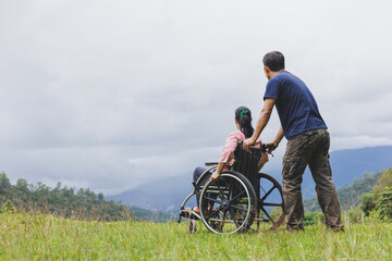 Male pushing wheelchair with disabled woman looking sky on mountain park