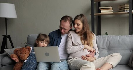 Young 35s couple with pregnant wife their little preschool daughter using laptop spend weekend at home. On-line content, educational program for kids, modern tech usage for purchasing or fun concept