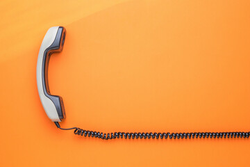 A gray handset with a wire on an orange background. Flat lay.