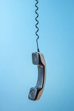 A gray retro phone handset suspended from a wire on a blue background.