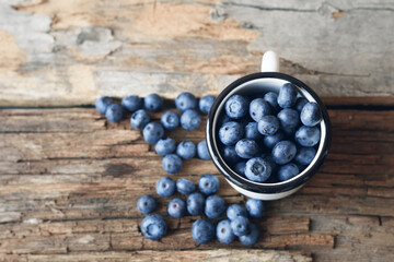 Blueberries in a white enameled mug on an old wooden table.