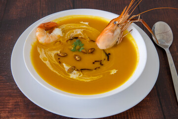 Pumpkin carrot ginger soup with prawn on wooden background