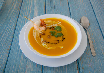 Pumpkin carrot ginger soup with prawn on wooden background