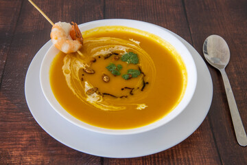 Pumpkin carrot ginger soup with prawn on wooden background