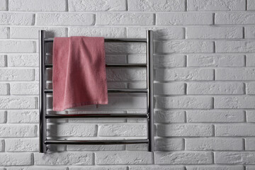 Modern heated towel rail with warm soft towel on white brick wall. Space for text