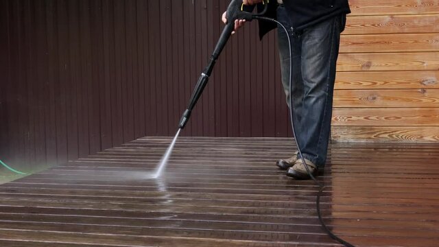 Man cleaning walls and floor with high pressure power washer. Washing terrace wood planks and cladding walls.