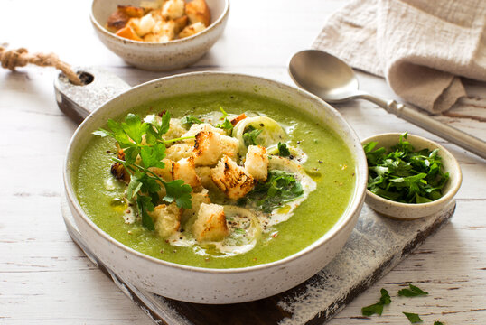 Creamy broccoli zucchini vegetarian soup with croutons in a bowl on white wooden background